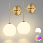 Two gold battery-operated wall sconces with milky white frosted glass shades mounted on a wall, illuminated with a warm glow.