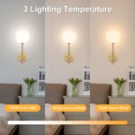Two gold battery-operated wall sconces with milky white frosted glass shades mounted on a wall, illuminated with a warm glow.